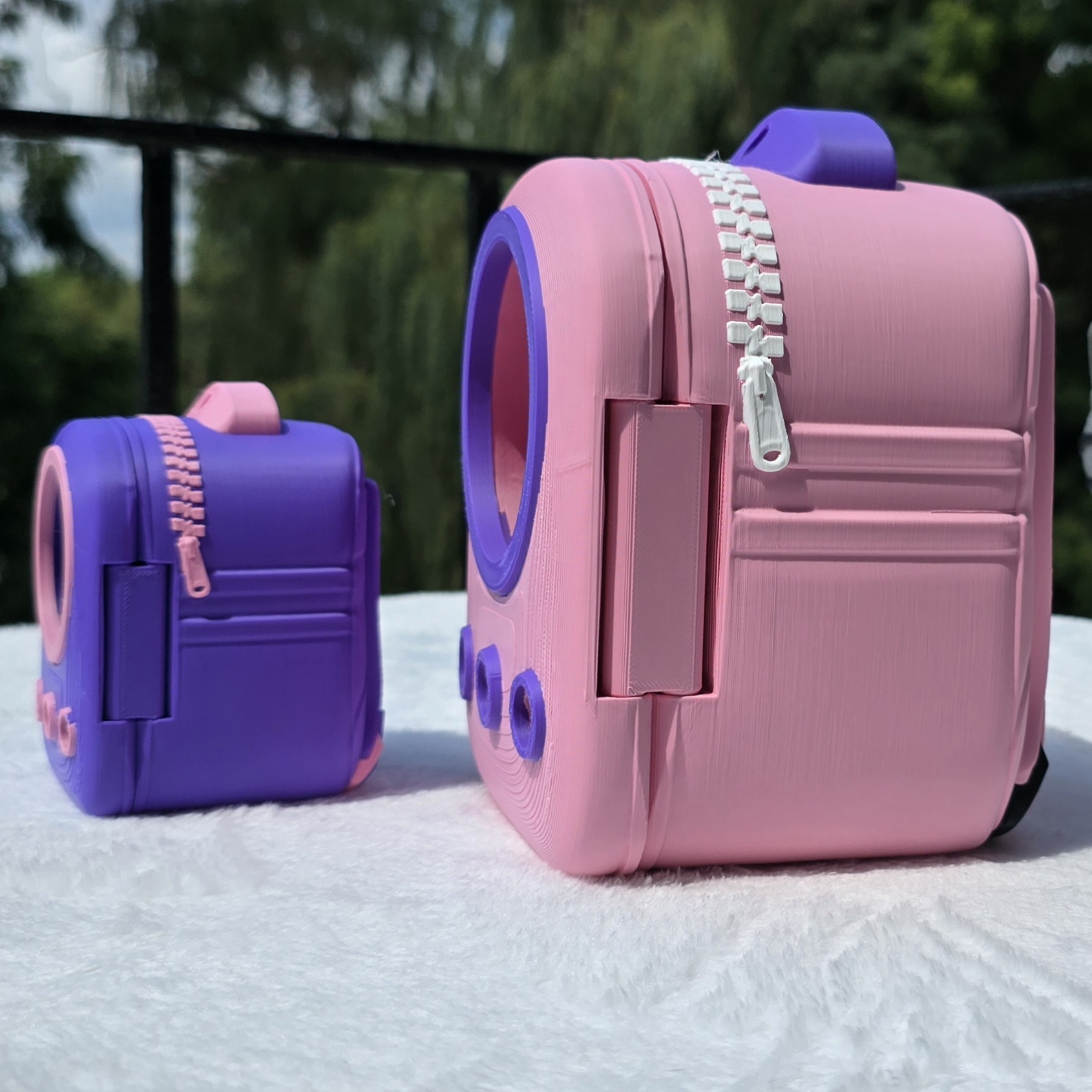 Pink and purple 3D printed cat backpacks at an angle showing the window ring, zipper pull, and air circles