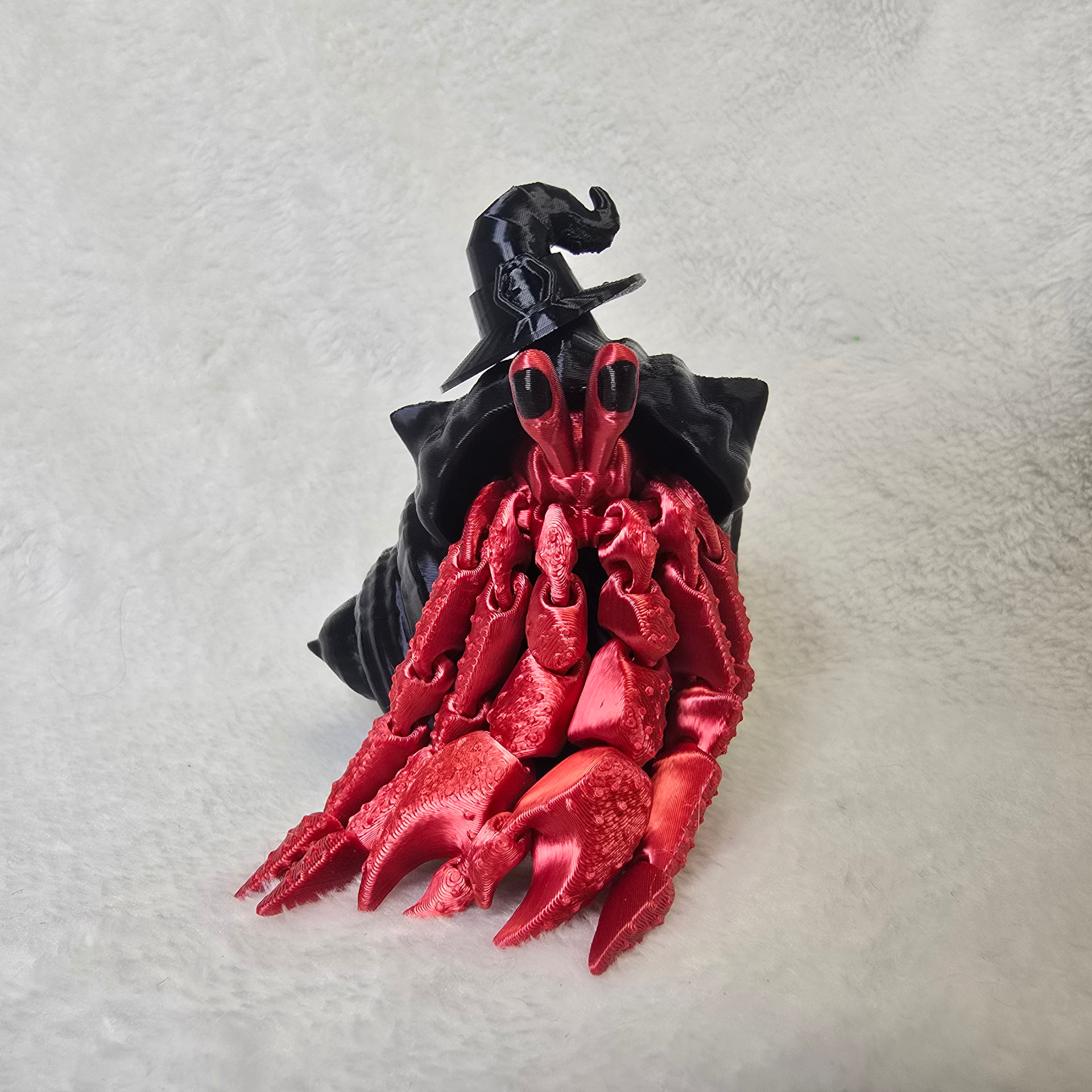 A red hermit crab in a black shell wearing a pointed witch hat