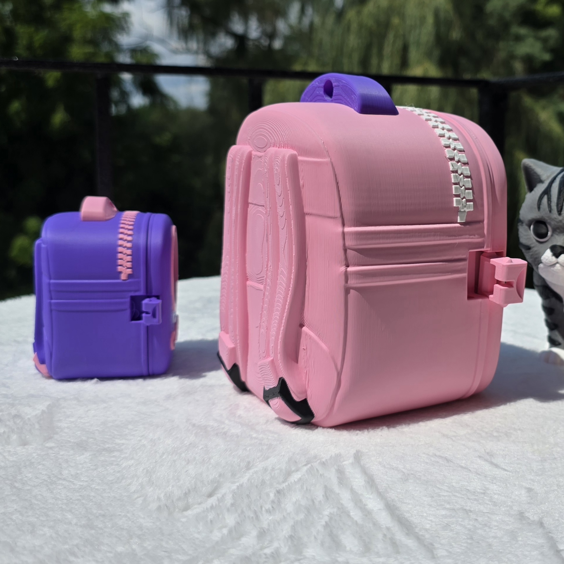 Side and back view of the pink cat backpack with the purple one behind it, showing the zipper