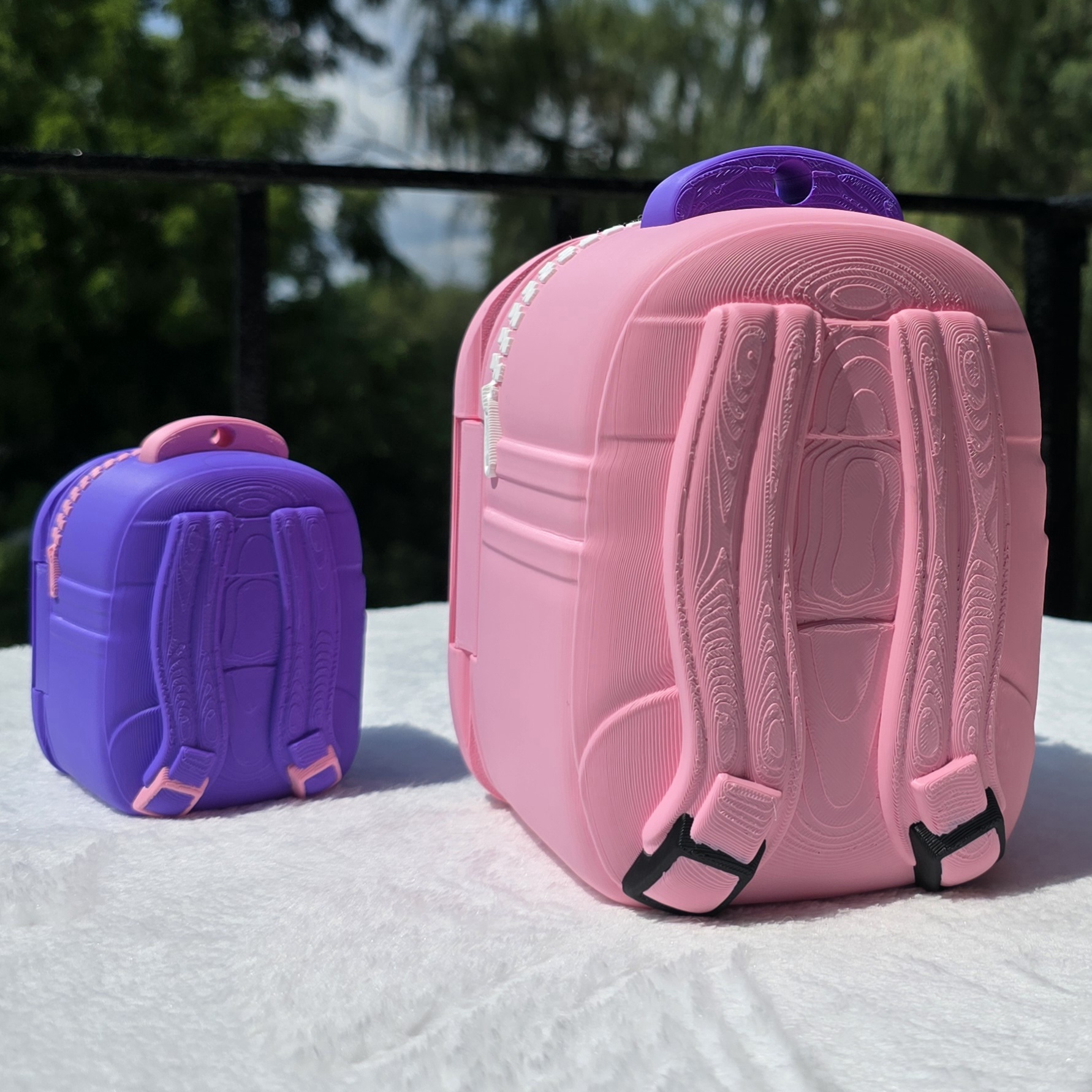 The backs of the pink and purple cat backpacks showing printed straps with black strap tips