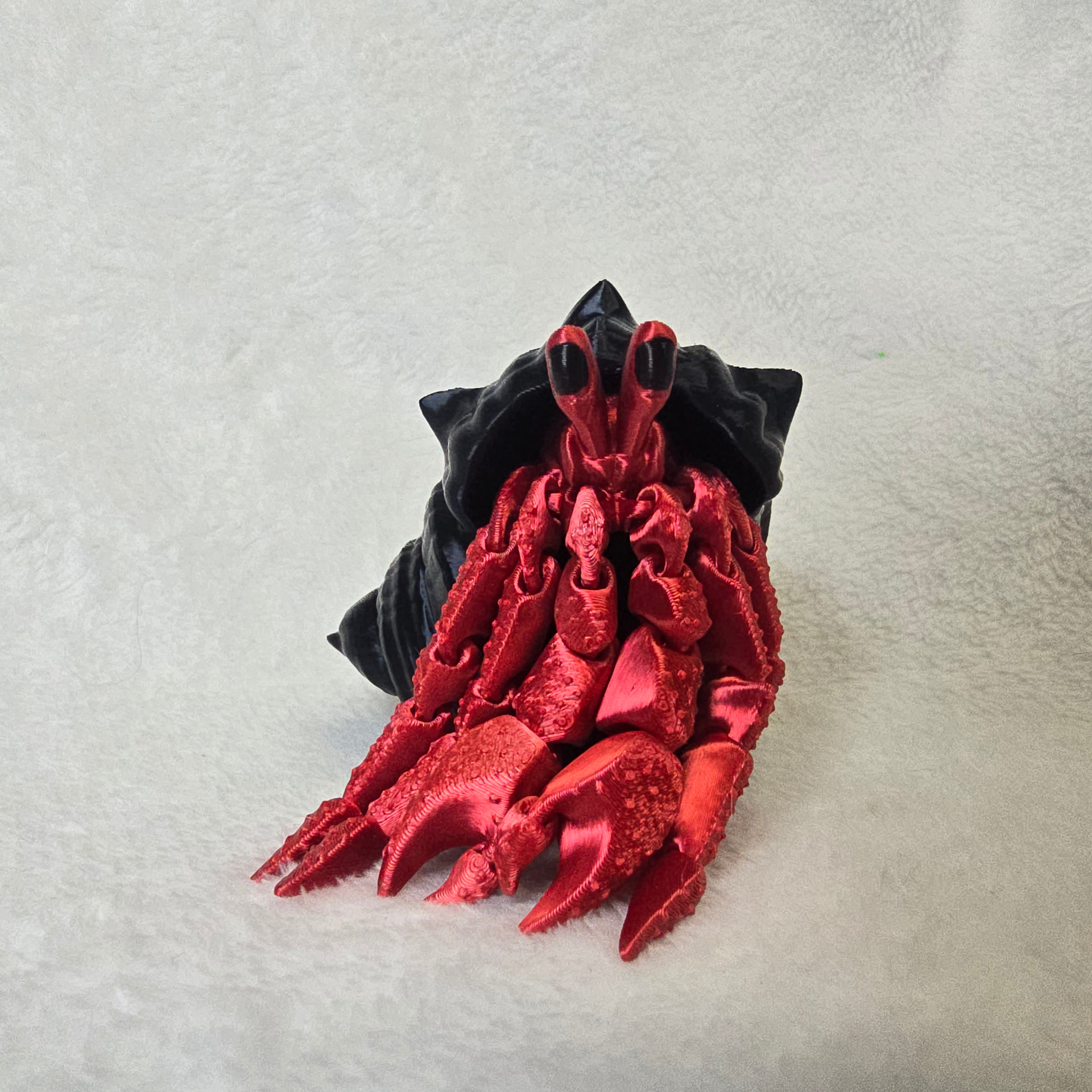 A red 3D printed hermit crab with articulated legs sitting in a black spiked shell